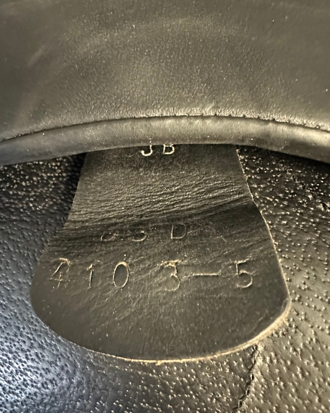 Close-up of a textured black leather tag with embossed text. Saddle